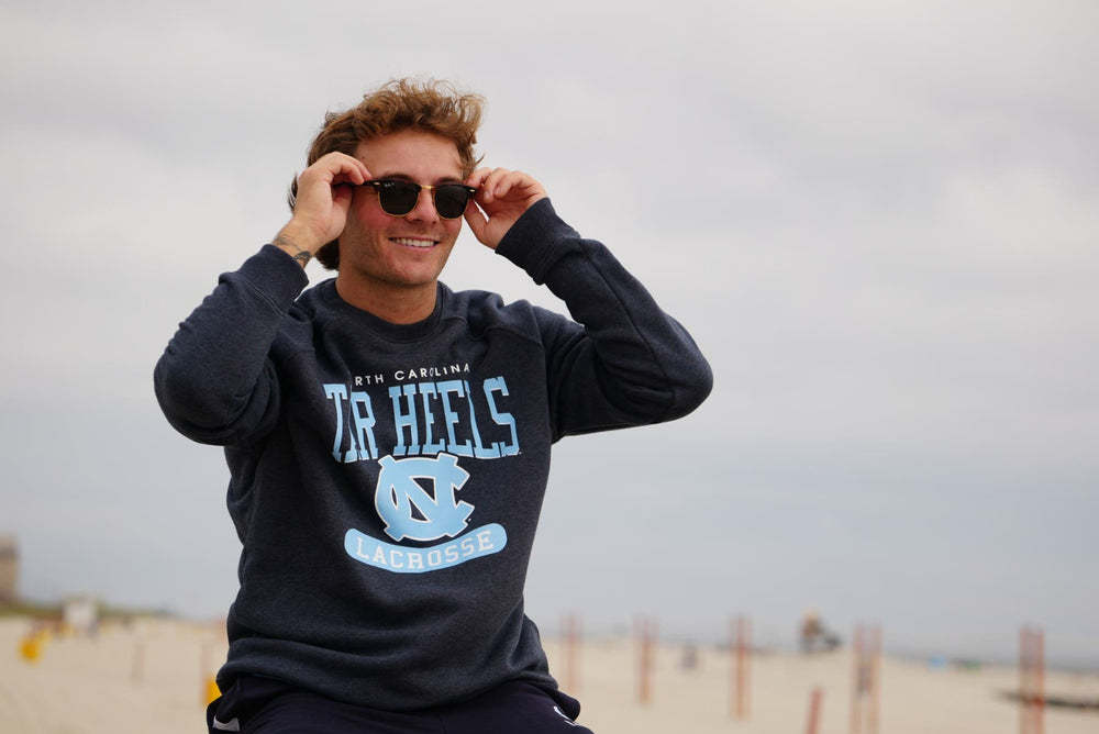 UNC Lacrosse crew neck on model with sunglasses sitting on the beach